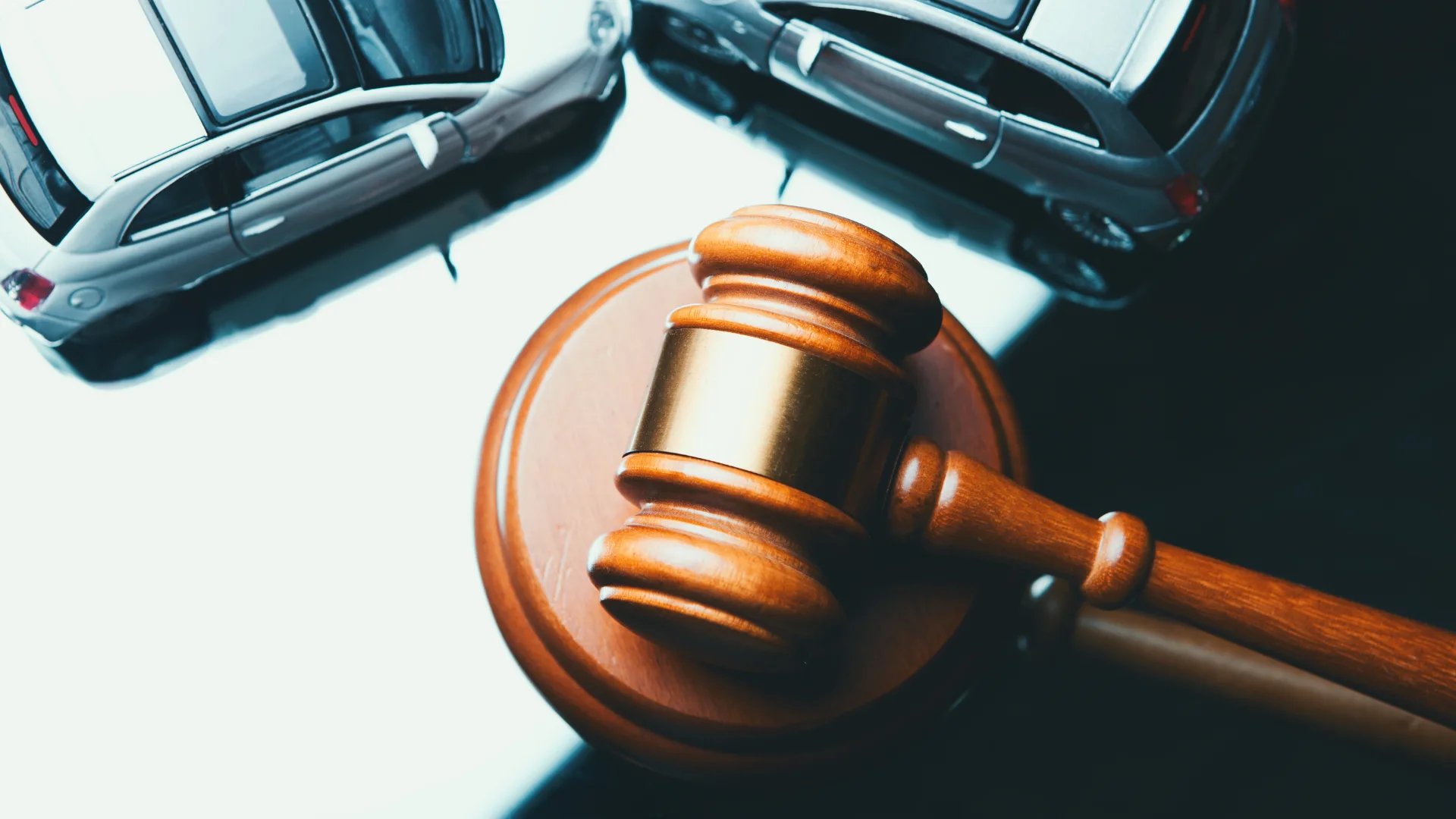 two toy cars on a desk that have collided and a gavel of justice next to them